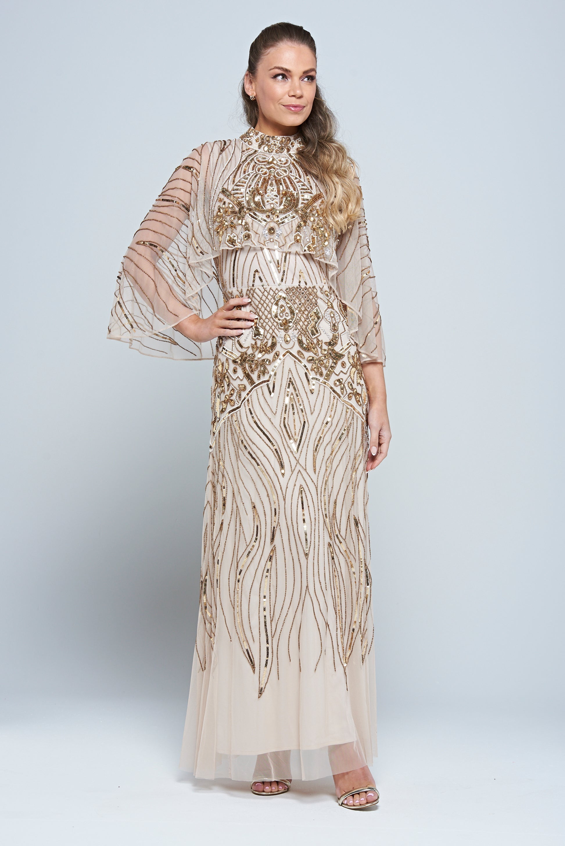 Celestine neutral-hued gold embellished maxi dress with flowing cape overlay, long sleeves, and modest elegant silhouette for weddings and formal occasions.