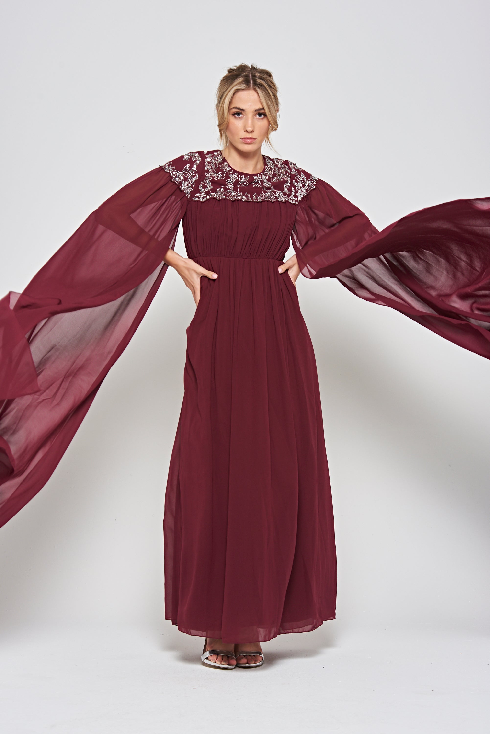 Frock & Frill Aruna burgundy embellished cape maxi dress with sparkling beaded bodice, flowing chiffon cape sleeves, and elegant full-length silhouette—ideal for weddings and formal events.
