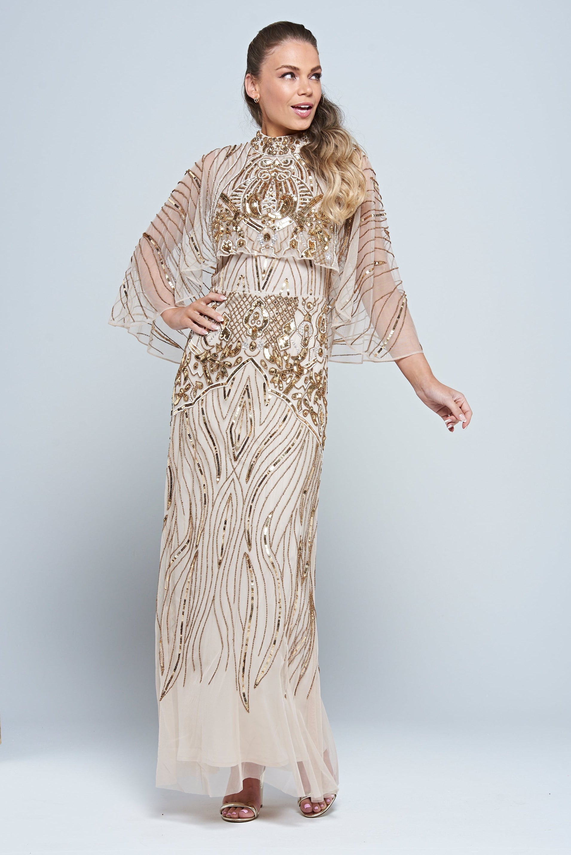 Celestine neutral-hued gold embellished maxi dress with flowing cape overlay, long sleeves, and modest elegant silhouette for weddings and formal occasions.
