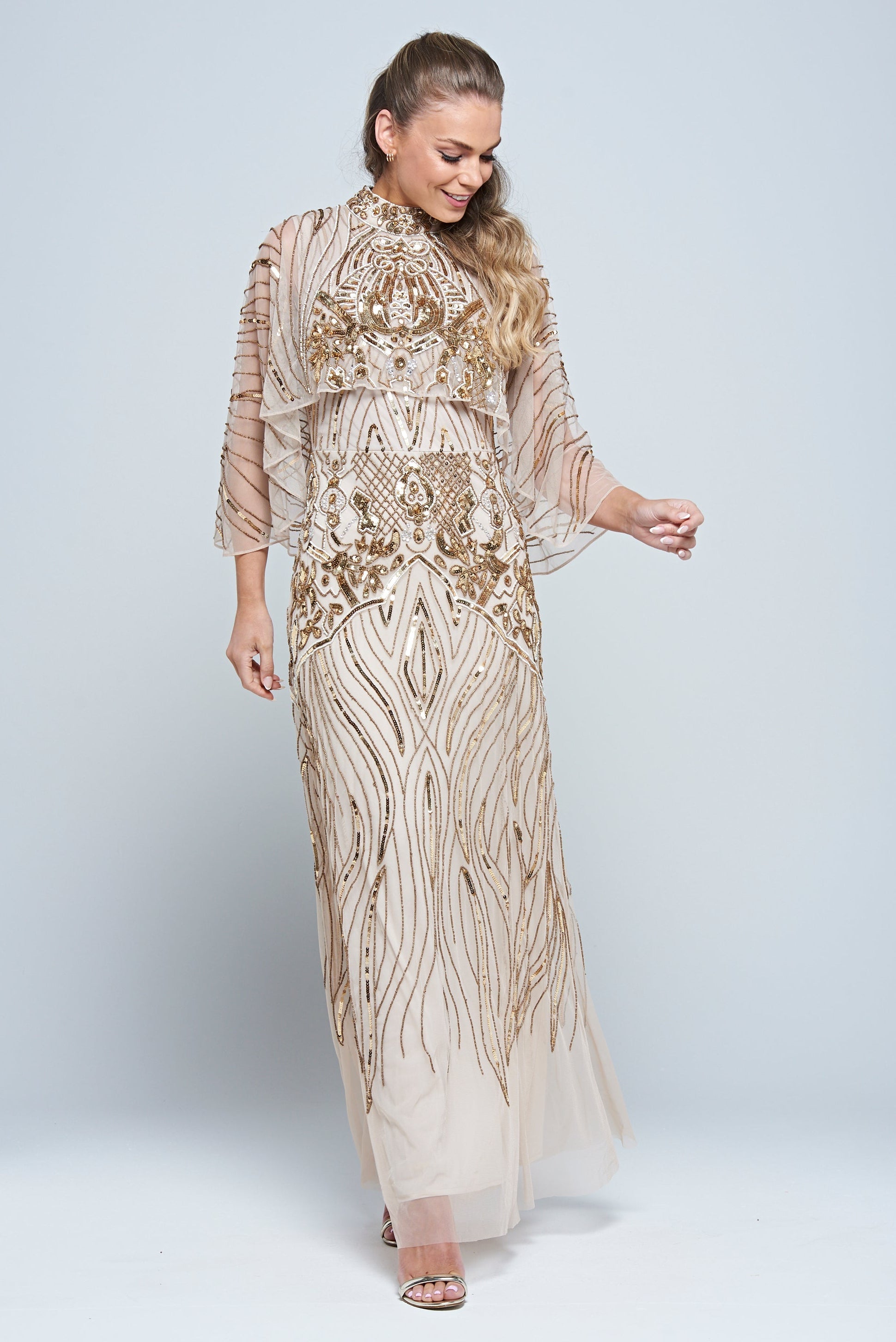 Celestine neutral-hued gold embellished maxi dress with flowing cape overlay, long sleeves, and modest elegant silhouette for weddings and formal occasions.