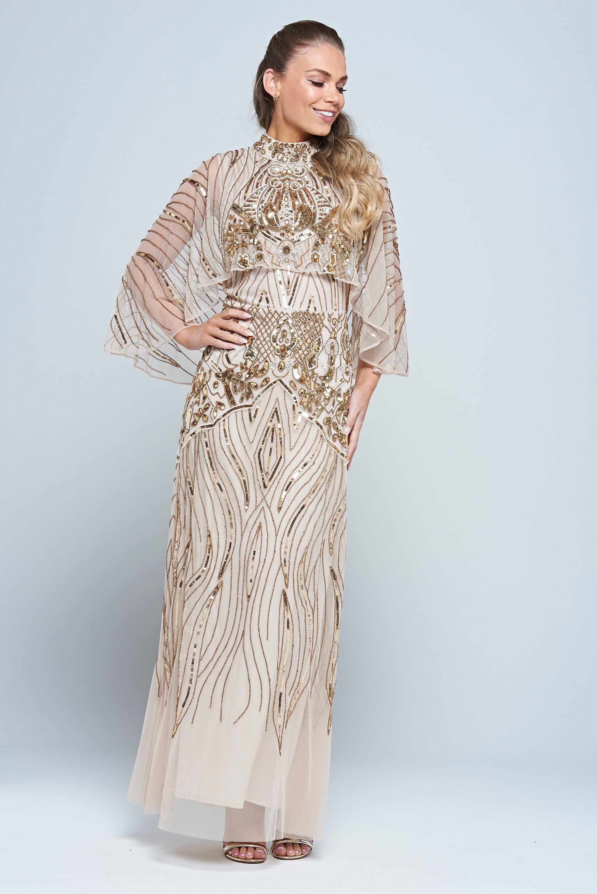 Celestine neutral-hued gold embellished maxi dress with flowing cape overlay, long sleeves, and modest elegant silhouette for weddings and formal occasions.
