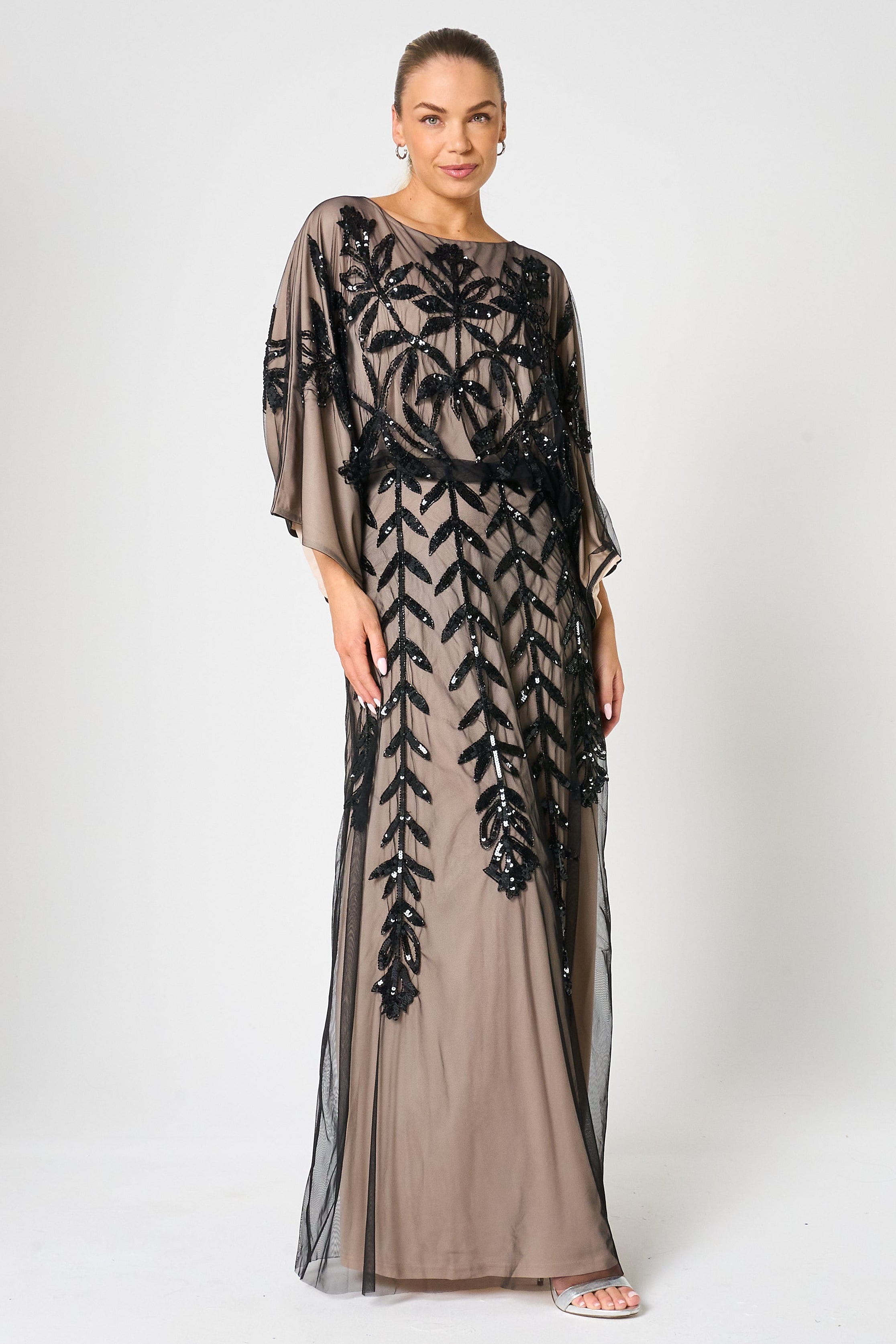 Elva sequin maxi dress with black leaf motif embellishment on a neutral base, batwing sleeves and flowing silhouette for statement occasion wear styling
