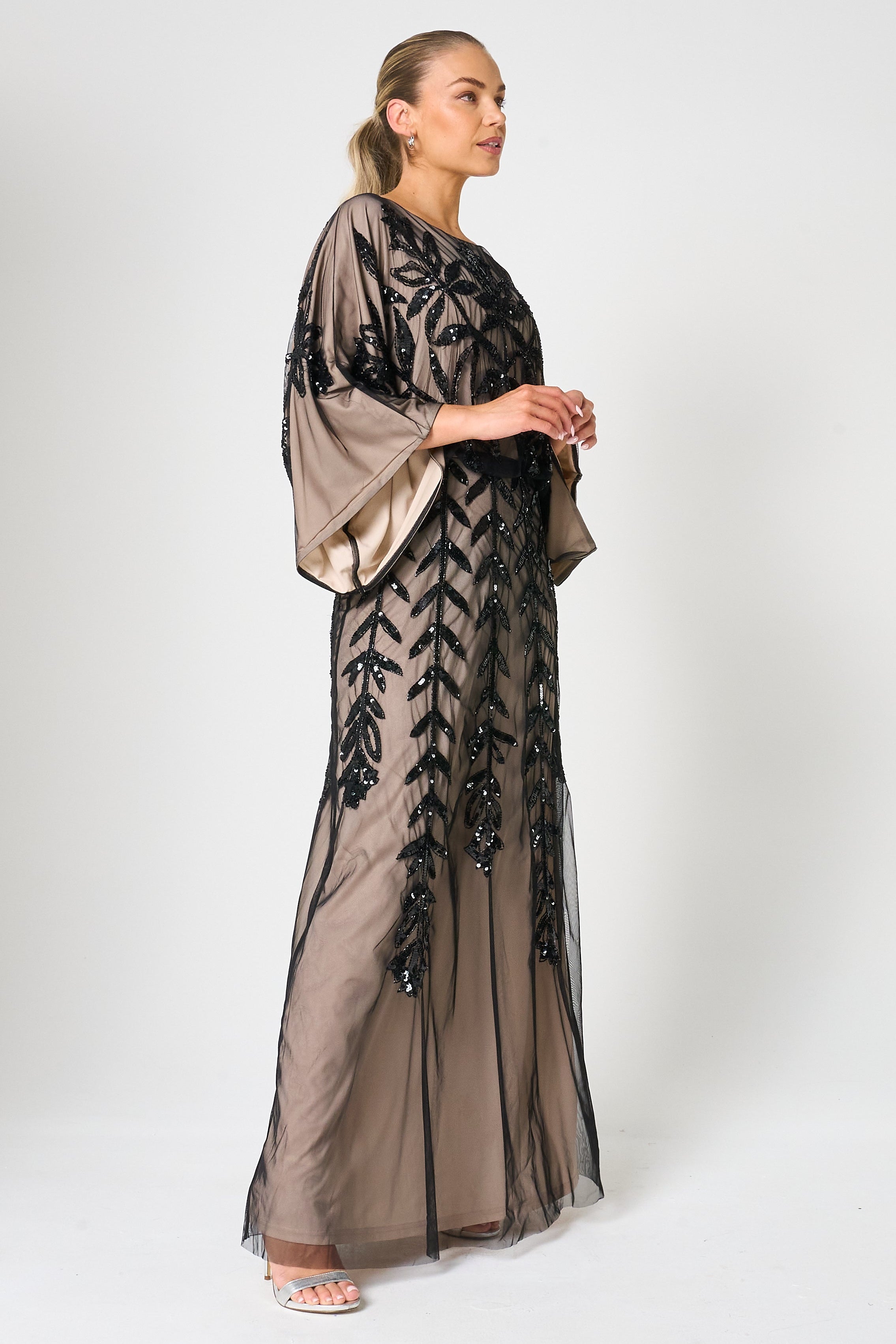 Elva sequin maxi dress with black leaf motif embellishment on a neutral base, batwing sleeves and flowing silhouette for statement occasion wear styling