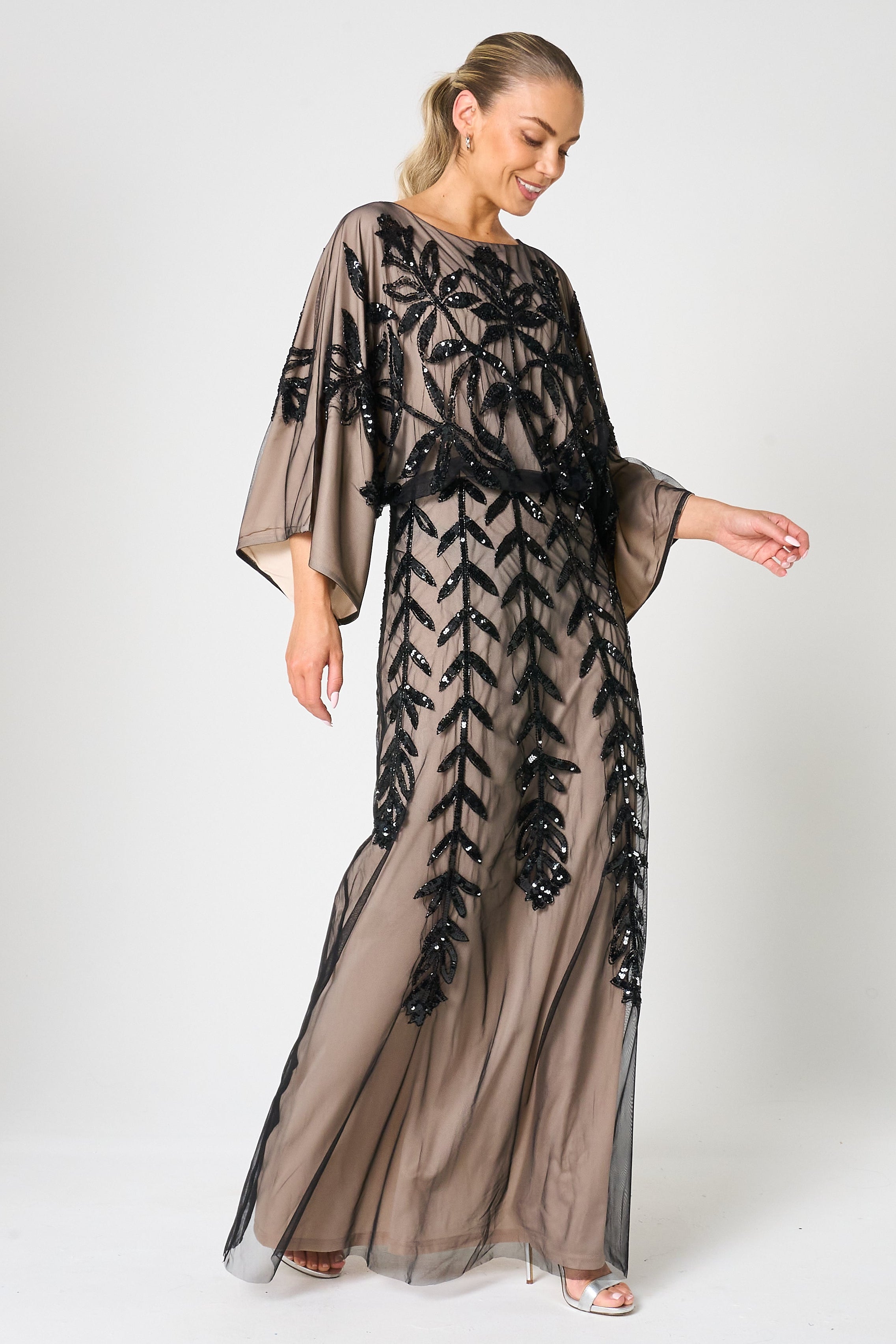 Elva sequin maxi dress with black leaf motif embellishment on a neutral base, batwing sleeves and flowing silhouette for statement occasion wear styling