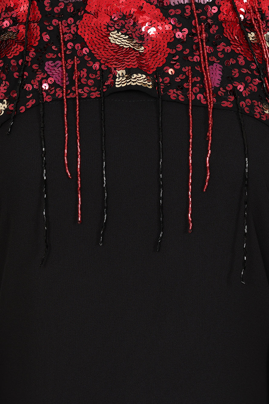 Elegant black maxi cape dress with a relaxed, fluid silhouette and a sheer flowing cape overlay that offers arm and shoulder coverage. The cape is decorated with deep red hand-sequinned floral motifs and cascading beaded tassels that add movement and spar