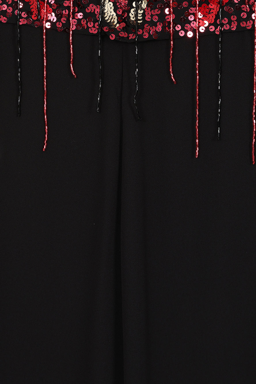 Elegant black maxi cape dress with a relaxed, fluid silhouette and a sheer flowing cape overlay that offers arm and shoulder coverage. The cape is decorated with deep red hand-sequinned floral motifs and cascading beaded tassels that add movement and spar