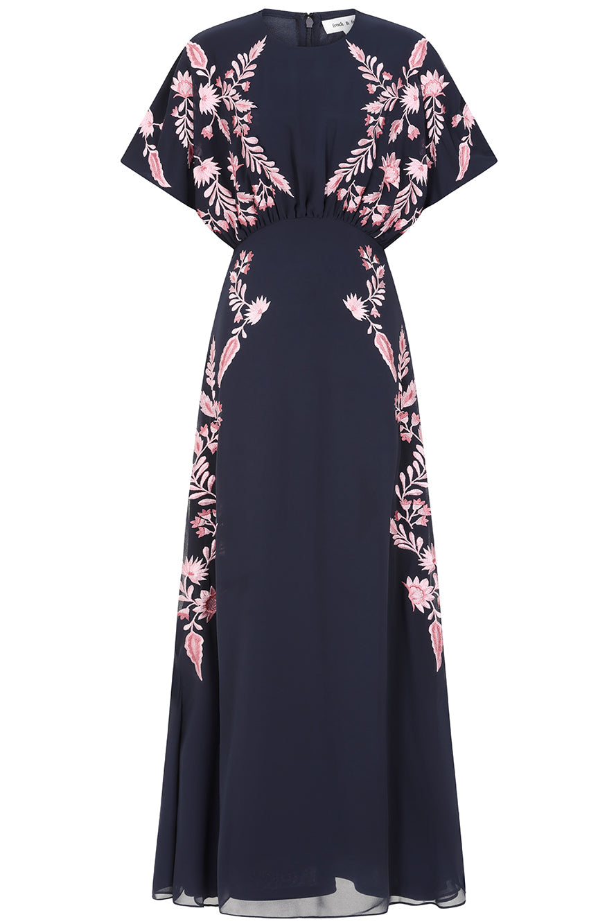 Navy floral embroidered maxi dress with pink detailing, worn by a model. Features flutter sleeves, a fitted waist and a flowing full-length skirt—perfect for weddings, evening occasions and special events.