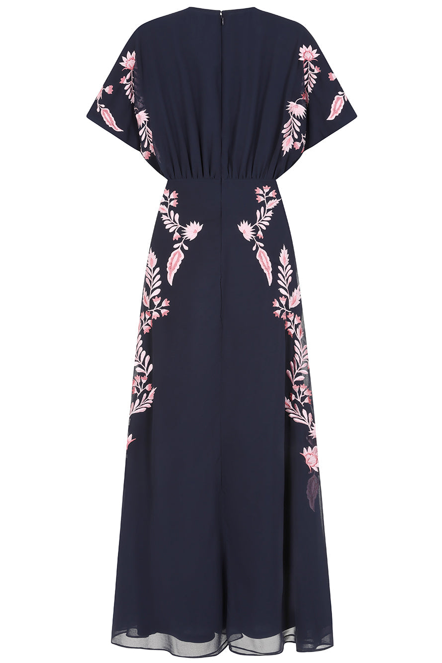 Navy floral embroidered maxi dress with pink detailing, worn by a model. Features flutter sleeves, a fitted waist and a flowing full-length skirt—perfect for weddings, evening occasions and special events.