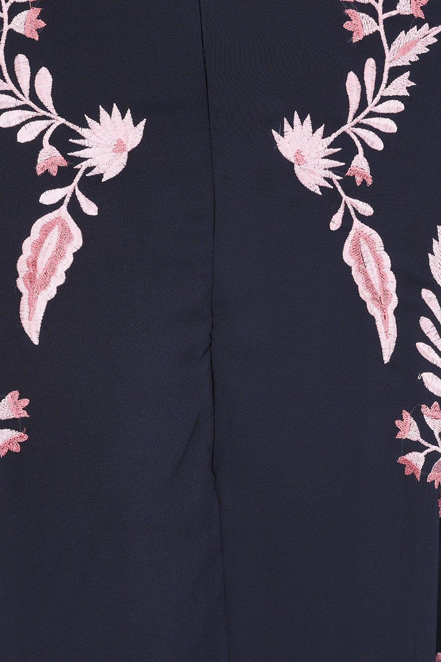 Navy floral embroidered maxi dress with pink detailing, worn by a model. Features flutter sleeves, a fitted waist and a flowing full-length skirt—perfect for weddings, evening occasions and special events.