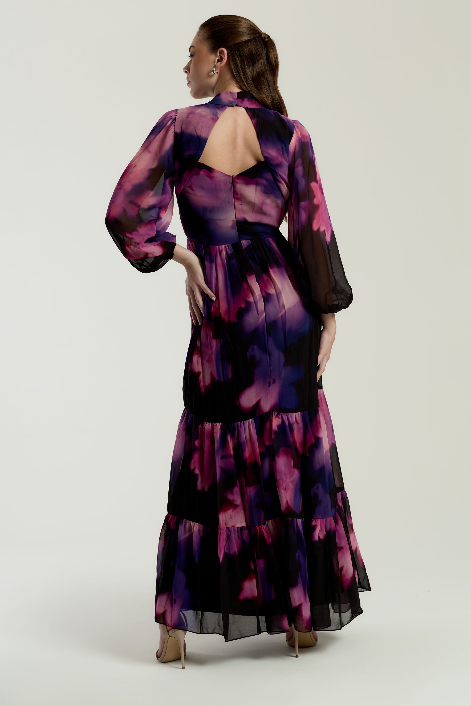 Black floral print maxi dress with high neckline, sheer long sleeves, tiered skirt and keyhole back detail displayed on a model.